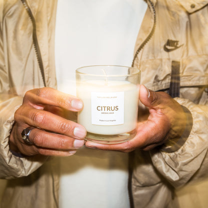 Person holding a candle labeled 'Citrus' in a neutral setting