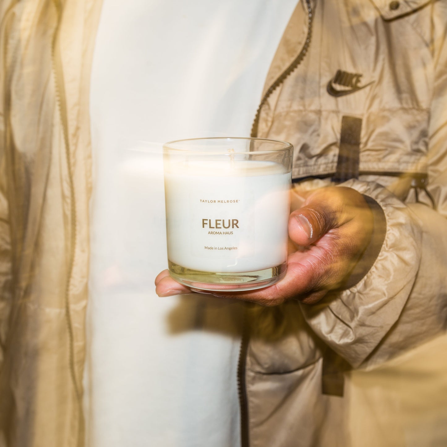 Person holding a candle labeled 'Fleur' in a neutral setting