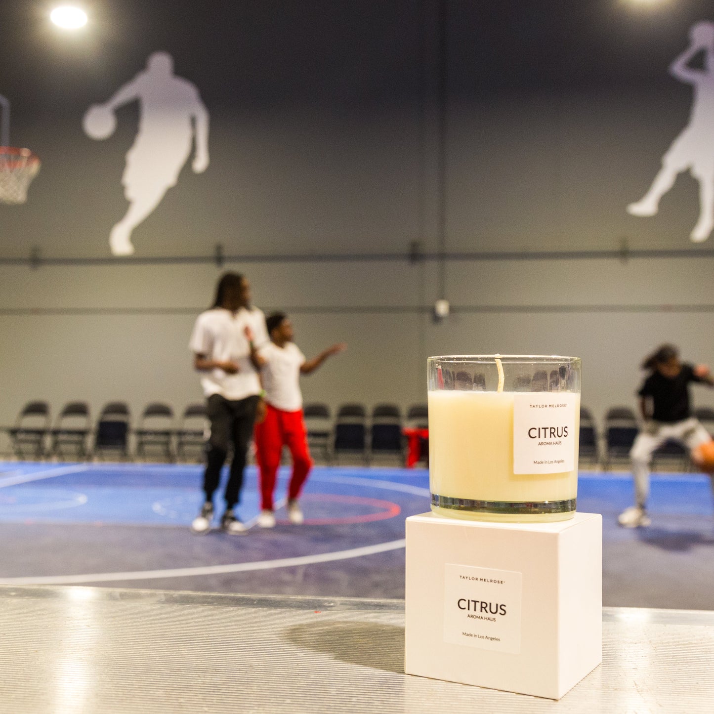 Candle labeled 'Citrus' on a basketball court with children playing basketball.